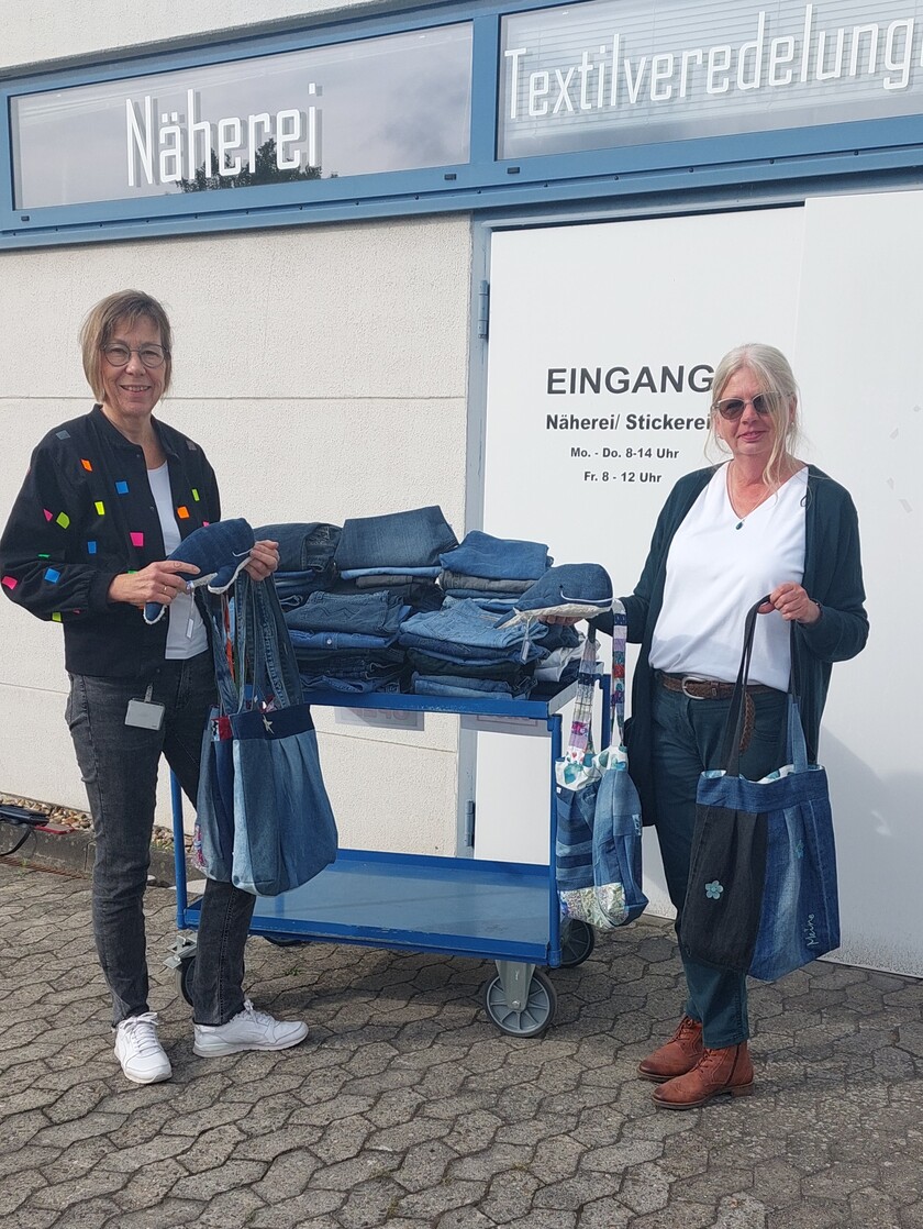 Unsere Mitarbeiterin der Unternehmenskommunikation überreicht die Jeansspende an die Leiterin der Näherei Lebenshilfe Wolfsburg.