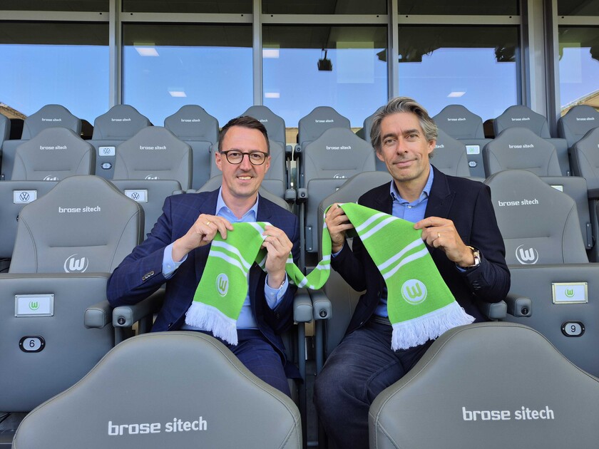 Michael Meeske, Geschäftsführung VfL Wolfsburg und Dalibor Dreznjak, Geschäftsführer der WOBCOM sitzen im Stadion und halten einen VfL-Wolfsburg Schal in die Kamera.