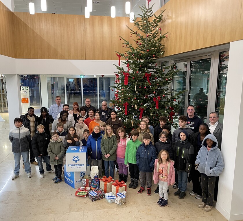 Die Kinder des Kinder- und Jugendschutz Wolfsburg e. V. des Tabaluga Kinderhaus stehen mit den Geschenken vor einem Weihnachtsbaum